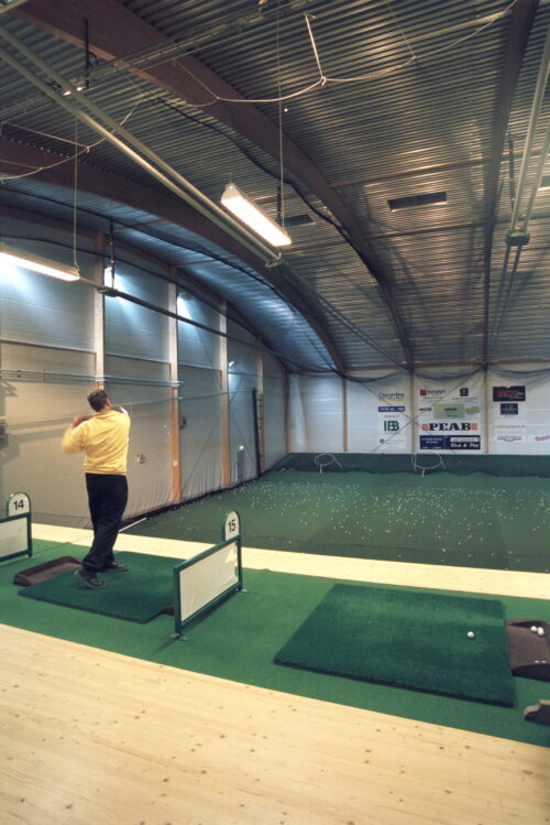 Driving range på insidan av en golfhall med limträstomme.